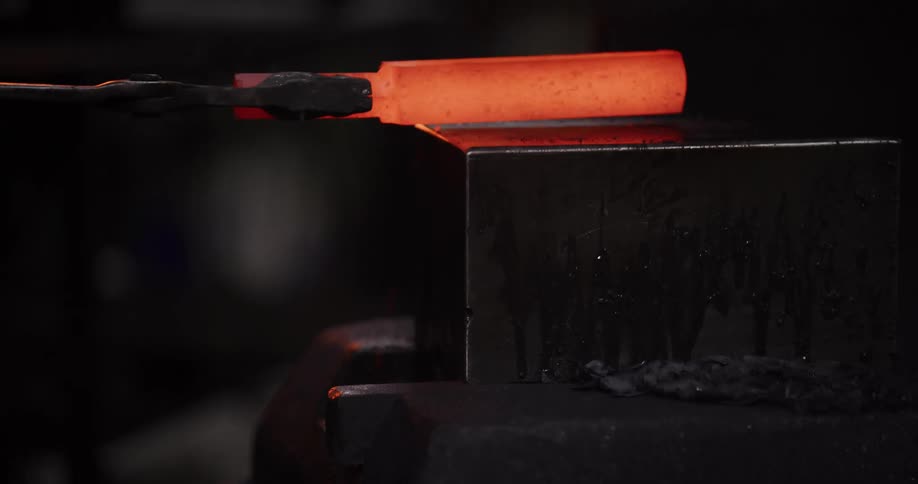 Close-up slow motion of a blacksmith placing a piece of red-hot metal on an anvil in a forge