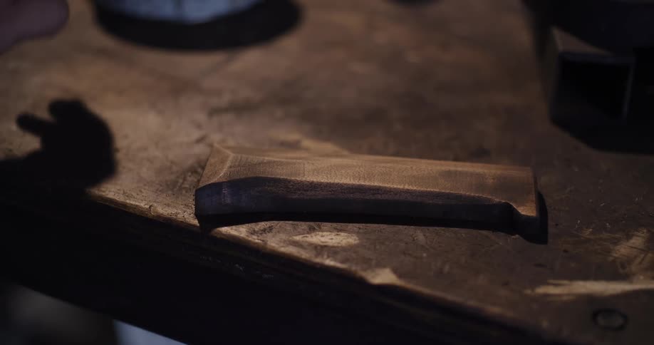 Close up shot of a craftsman's tattooed hands with silver rings sanding and painting a piece of wood in a workshop