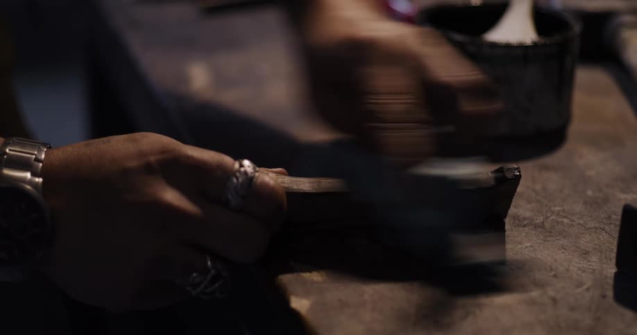 Close up of a skilled artisan's hands carefully applying a dark stain to a piece of wood in a dimly lit workshop