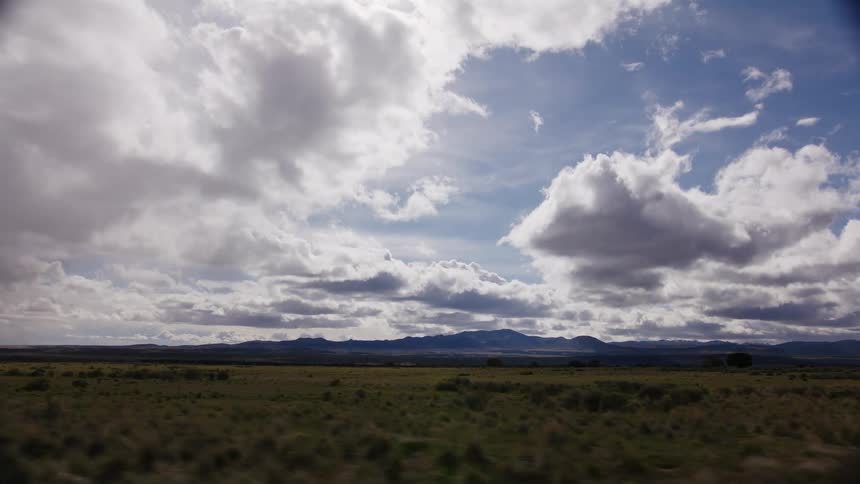 A beautiful moving shot travels through a vast, open prairie with dramatic clouds filling the sky and distant mountains on the horizon