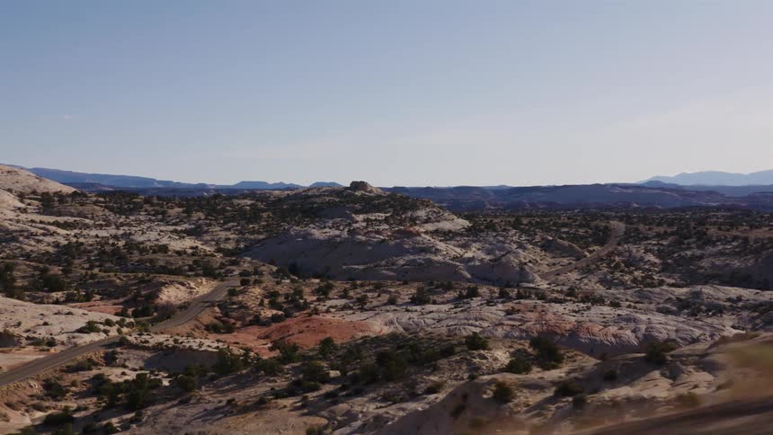 POV shot while driving along a scenic highway through the vast, rocky desert terrain of Utah on a clear day