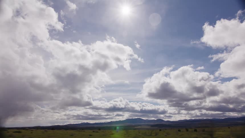 A beautiful tracking shot captures the expansive green landscape under a sunlit cloudy sky with distant mountains