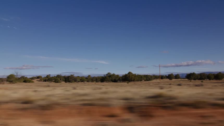 A side-view shot from a fast-moving vehicle captures the blur of a sunny, arid landscape with sparse trees and distant mountains