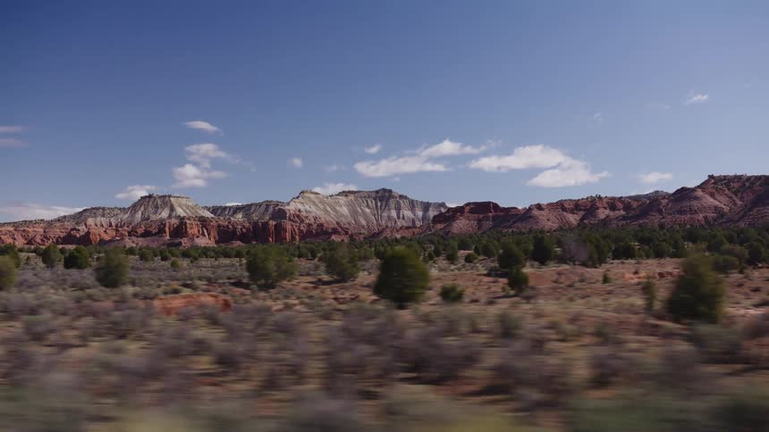 A scenic drive through a vast desert reveals stunning red and white rock formations and mountains under a clear blue sky