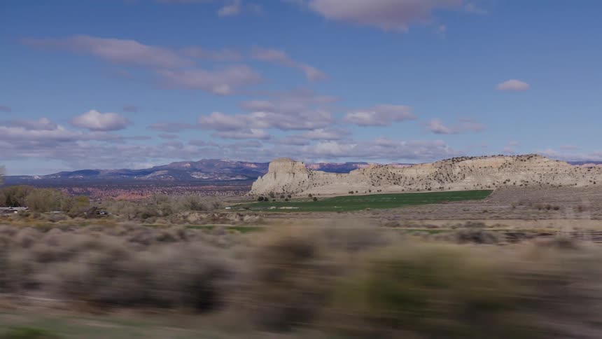A scenic drive through a vast desert valley reveals green farmland nestled against majestic rock formations