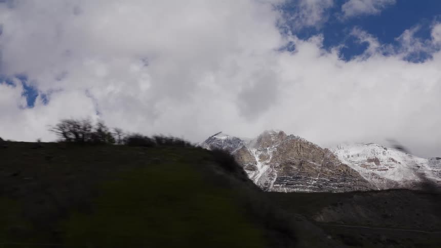 A majestic snow-capped mountain range is seen from a scenic drive on a partly cloudy day