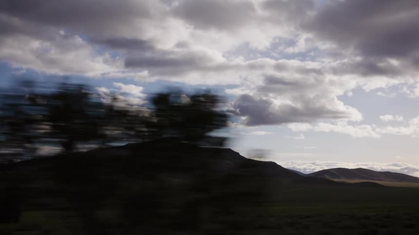 A beautiful slow-motion drive-by shot of a vast mountain range with green fields under a cloudy sky