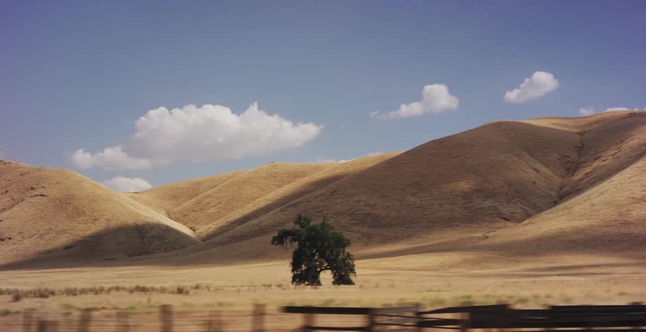 A cinematic tracking shot pans across golden rolling hills before revealing a couple driving a classic silver Mustang down a remote country road