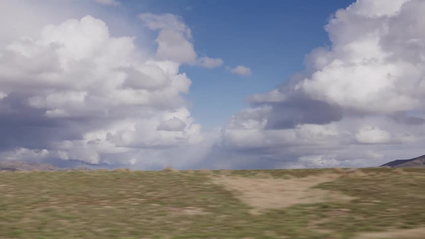 A high-speed driving plate shot shows a vast, arid landscape with distant mountains under a dramatic sky with rain clouds on the horizon