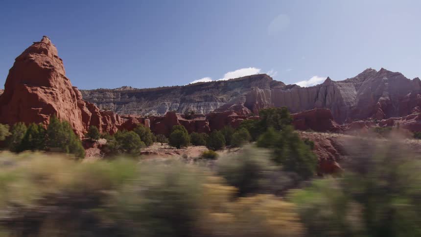 A scenic tracking shot passes stunning red rock formations in a vast desert landscape on a bright, sunny day
