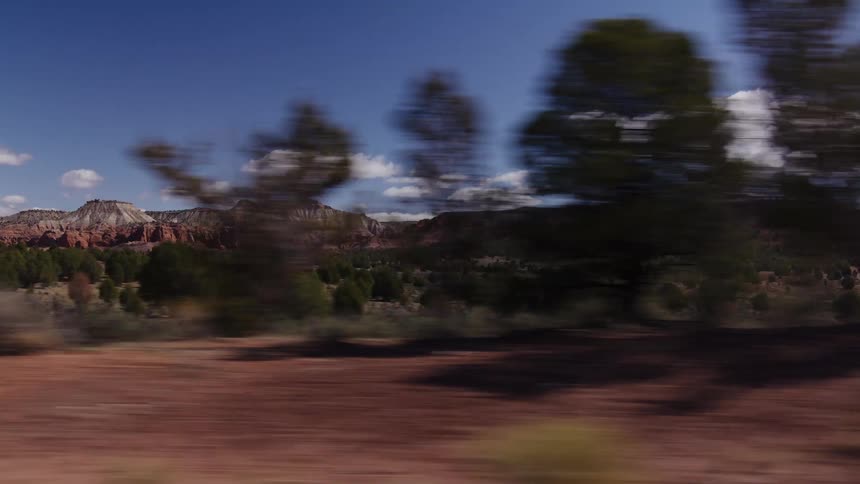 Side-view from a moving vehicle captures the magnificent red rock mountains and desert landscape on a sunny day