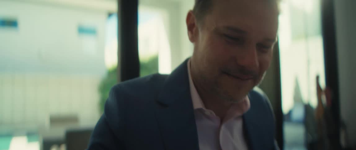 A happy businessman in a suit smiles as he works at his desk, using a calculator to review financial documents