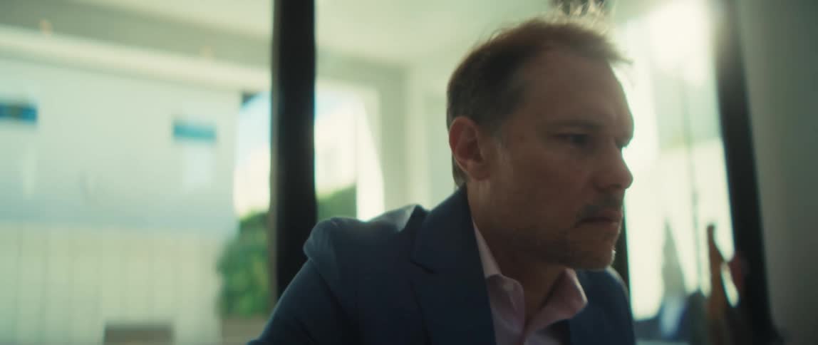 A serious businessman in a suit carefully writes on a document at his desk in slow motion