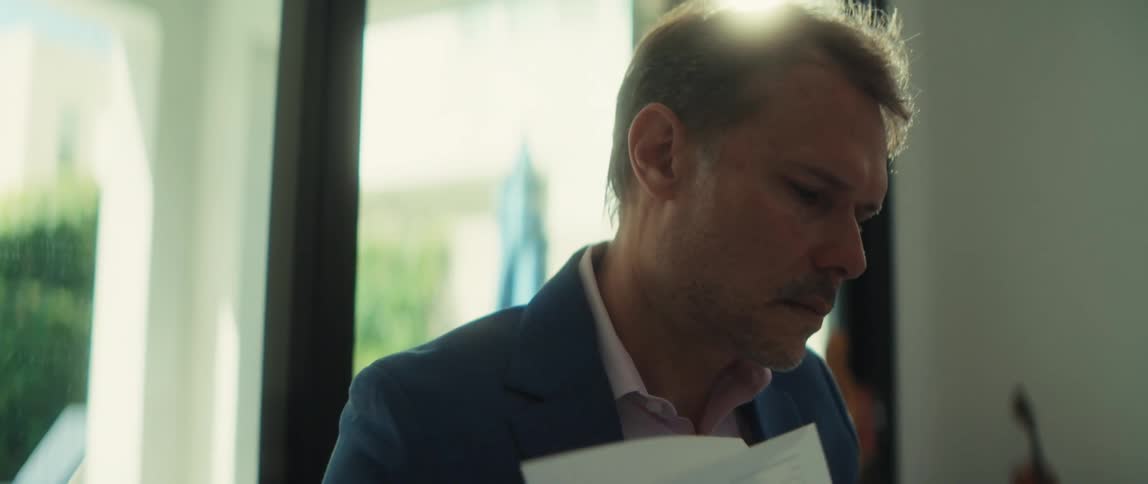 A businessman in a suit carefully reviews paperwork at his sunlit desk