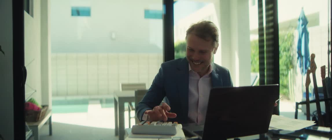 A successful businessman smiles with satisfaction while working on his laptop in his bright, modern home office