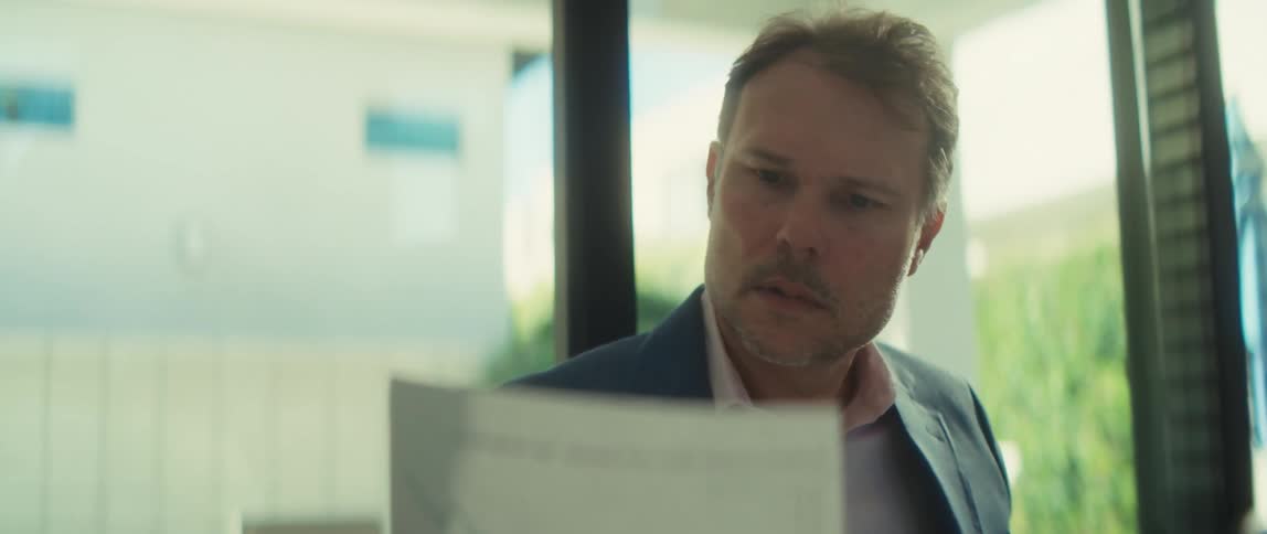 A concerned businessman in a modern, sunlit office reacts with worry while analyzing a document with a downward trending graph