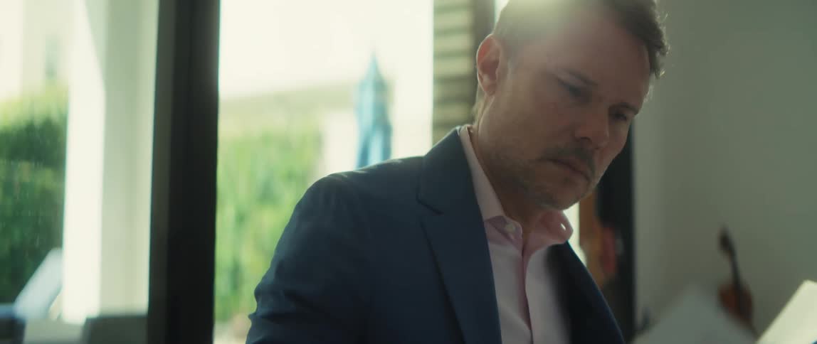 A focused businessman in a blue suit carefully reviews a stack of important documents in a sunlit office