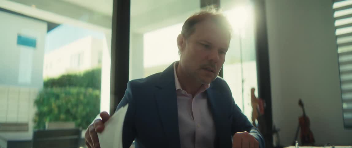 A serious businessman carefully reviews important documents at his modern desk, putting on his glasses to focus in a slow-motion shot
