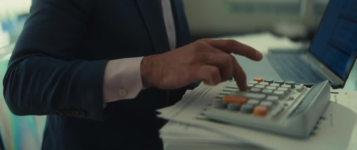 A focused businessman meticulously works on his finances, using a calculator at his desk in a corporate office