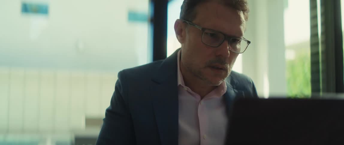 Slow motion shot of a serious businessman putting on his glasses to better see his laptop screen while working from home