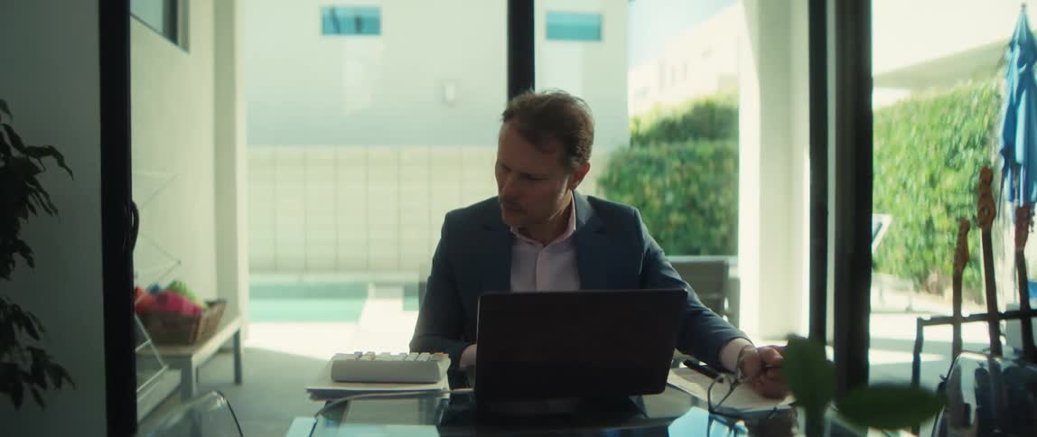 A dedicated businessman with earbuds works on his laptop in a bright, modern home office