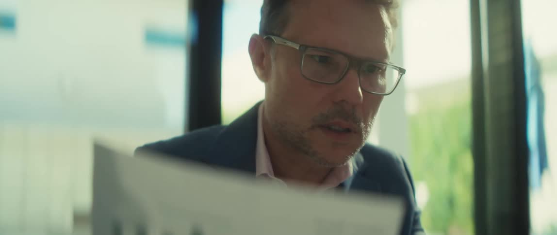 A businessman wearing glasses carefully analyzes a financial bar chart while working on his laptop in a modern office