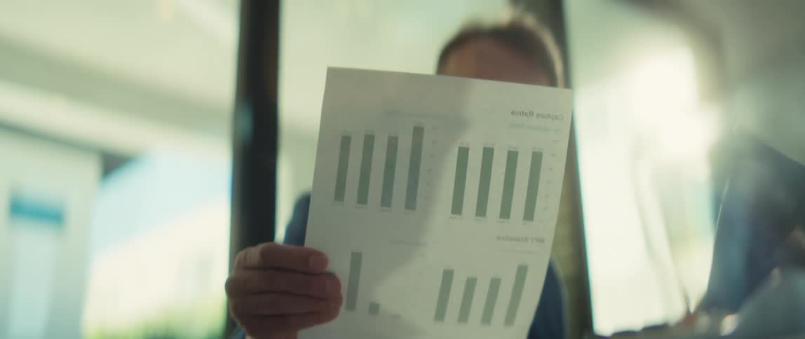 A serious businessman in a suit and glasses analyzes a financial report with bar charts in a bright office
