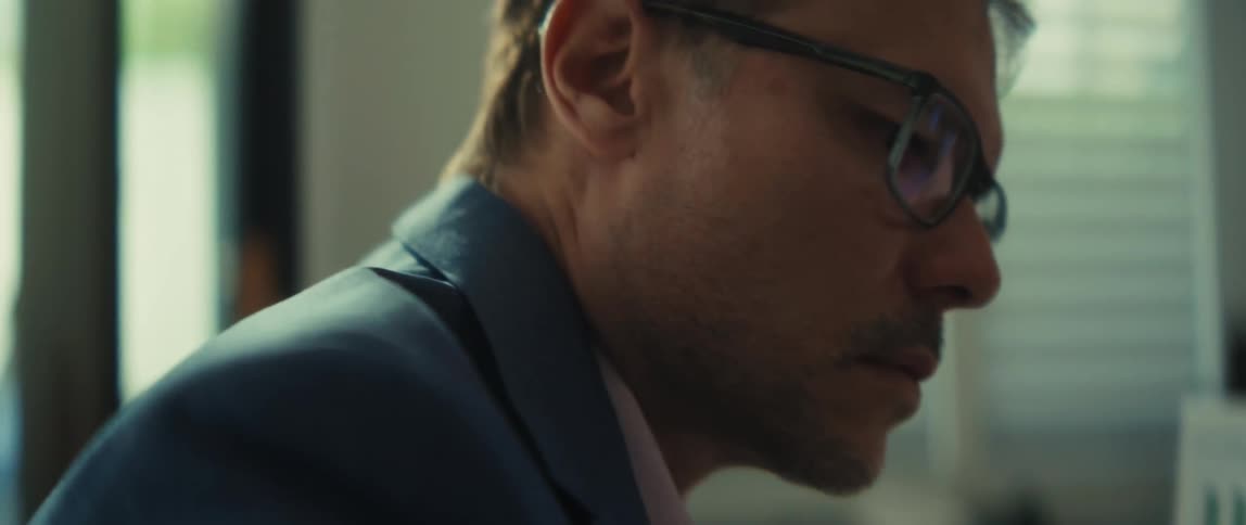 A businessman in a modern office analyzes financial data, comparing a printed bar graph report to a spreadsheet on his laptop