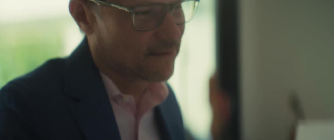 A focused businessman wearing glasses carefully reviews a financial bar graph in a brightly lit office setting