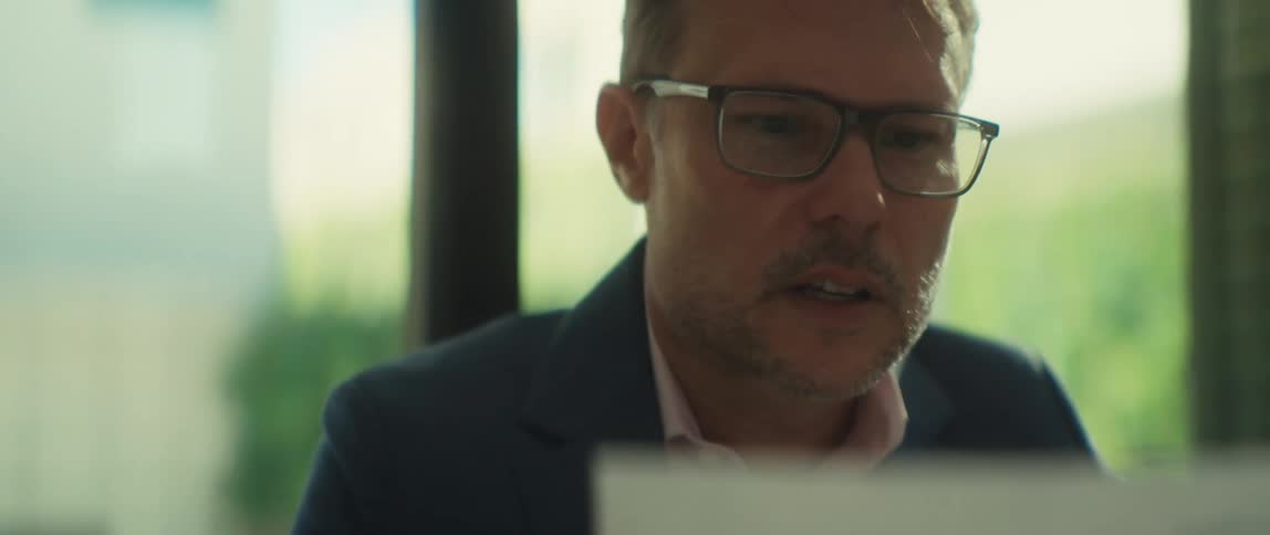 A close-up of a focused businessman in glasses concentrating while working in a brightly lit office