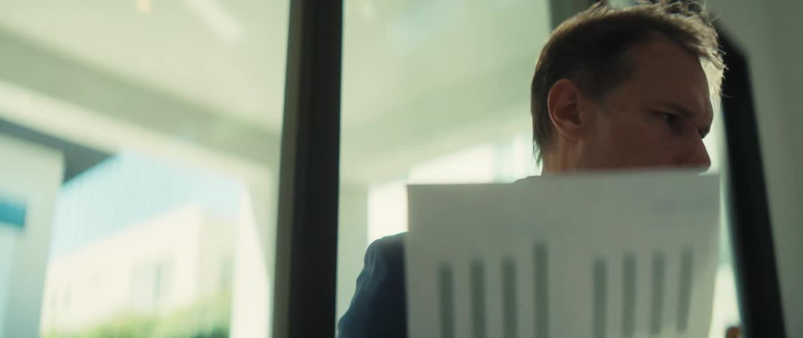 A serious businessman in a suit intently analyzes a financial report with bar charts in a bright, sunlit office