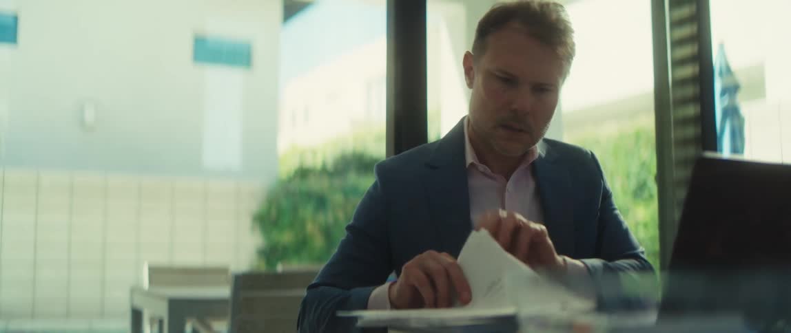 A serious businessman diligently reviews financial documents with charts and graphs while working on his laptop in a modern, sunlit office