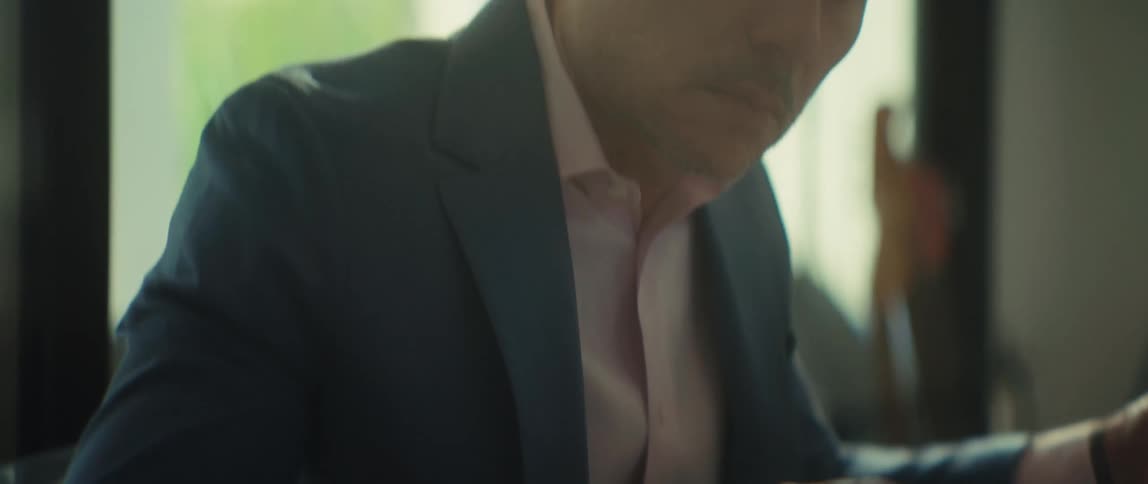 A mature businessman in a suit intently calculates numbers on a calculator while reviewing paperwork in his office