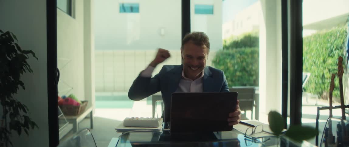 Excited professional businessman pumps his fist in victory after receiving good news on his laptop while working from his modern home office