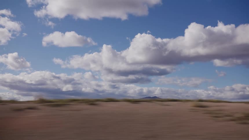 A beautiful, fast-moving view of a vast desert landscape with mountains on the horizon under a dramatic, cloudy blue sky