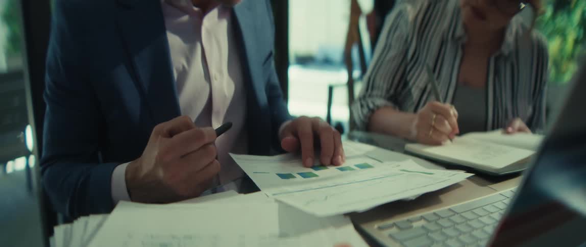 Close-up shot of a businessman pointing at a chart and explaining financial data to a woman taking notes