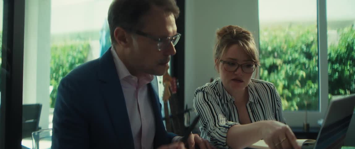 A businessman and a businesswoman with glasses intently review work on a laptop during a meeting in a bright, modern office