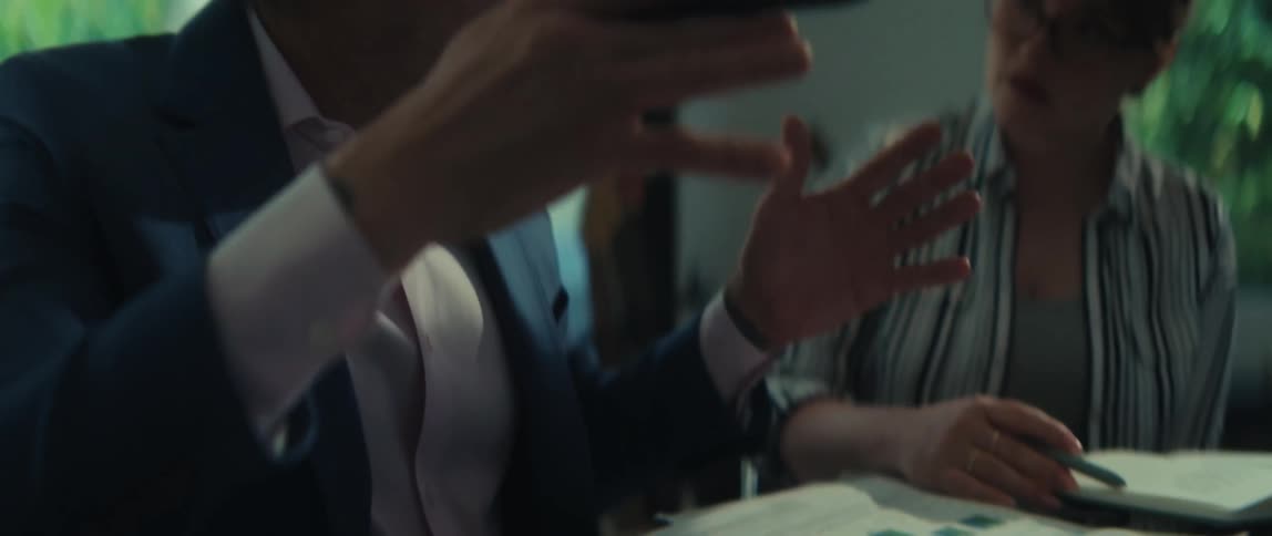 Slow-motion close-up of a businessman in a suit explaining company growth from a chart to a female colleague