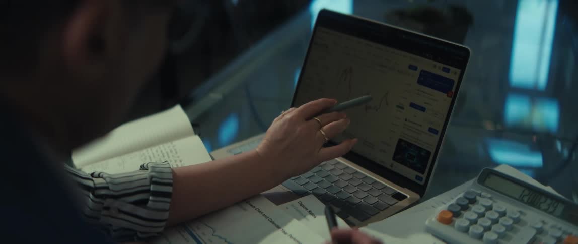 An over-the-shoulder view of two colleagues collaborating and analyzing financial charts on a laptop at a desk