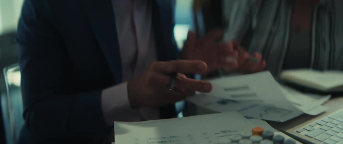 Close-up of a businessman's hands as he reviews financial charts and data with a colleague during a meeting