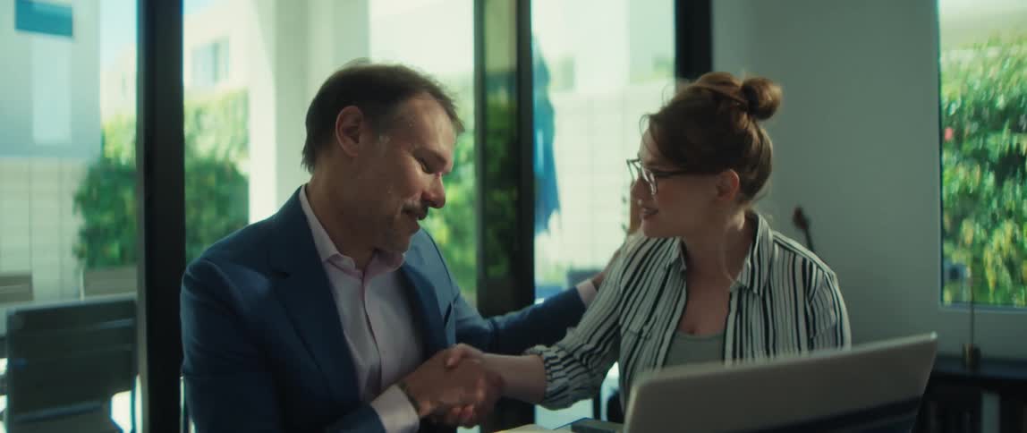 A professional businessman and businesswoman happily shake hands to close a deal during a meeting in a bright office