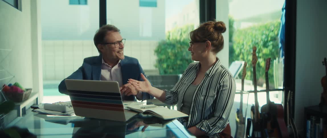 A professional man and woman smile and shake hands after a successful business meeting in a modern home office
