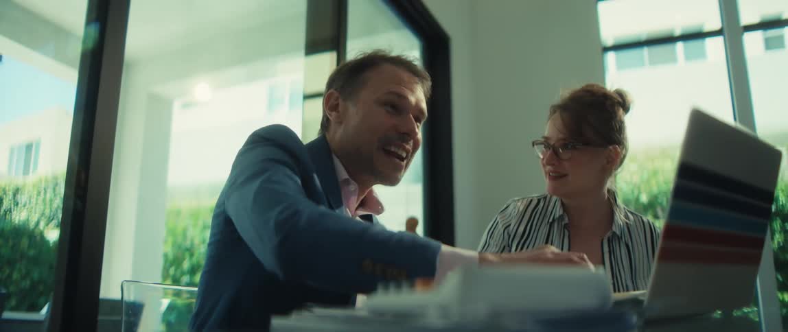A businessman and his female colleague animatedly discuss a project on a laptop, culminating in an excited gesture of success