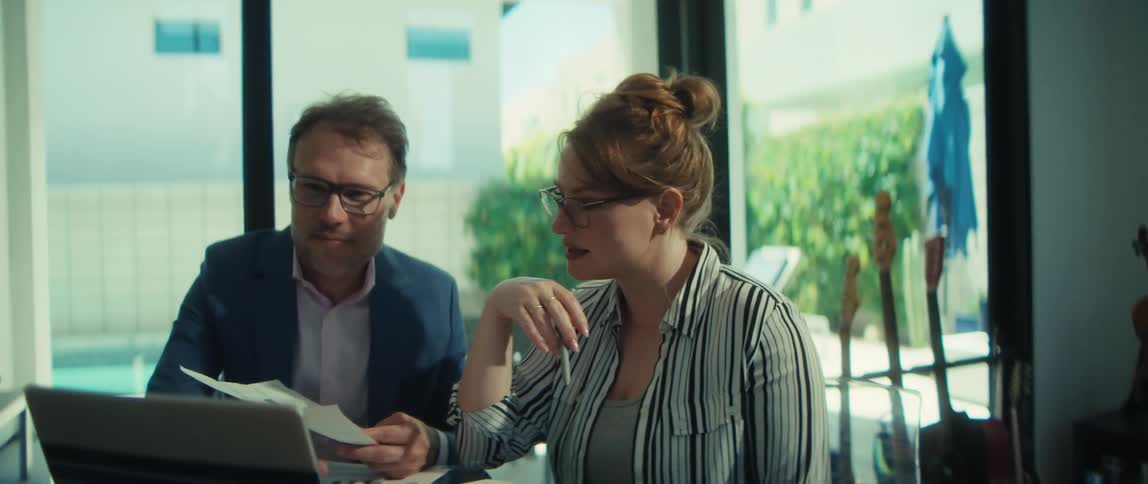 Two business professionals collaborate on a project, reviewing documents and using a laptop in a bright, modern office space