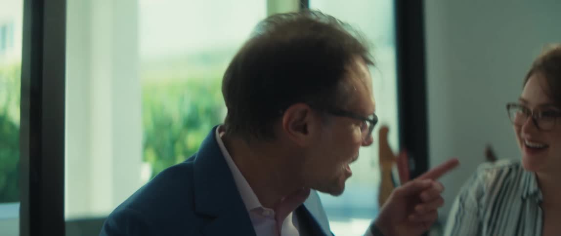 Two cheerful colleagues in a modern office collaborate on a project, with the man animatedly explaining details on a laptop to his coworker