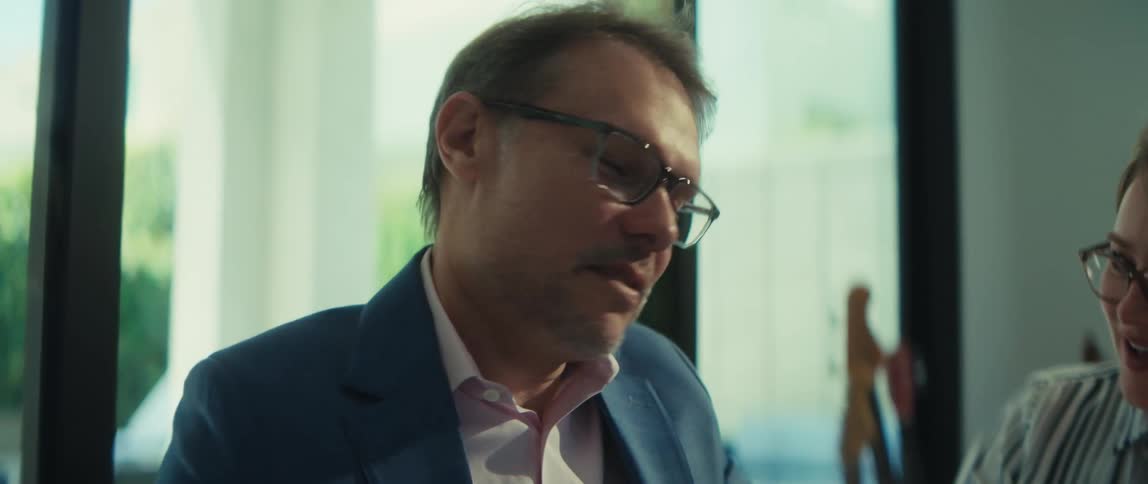 Two smiling professionals in glasses discuss business documents and charts in a bright, modern office