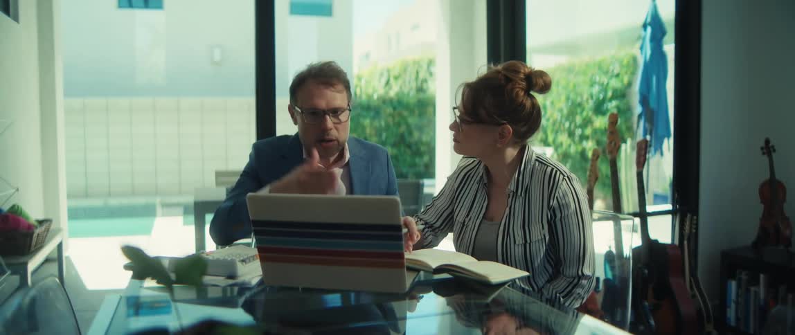 A man and a woman in business attire collaborate on a laptop during a meeting in a bright, modern office