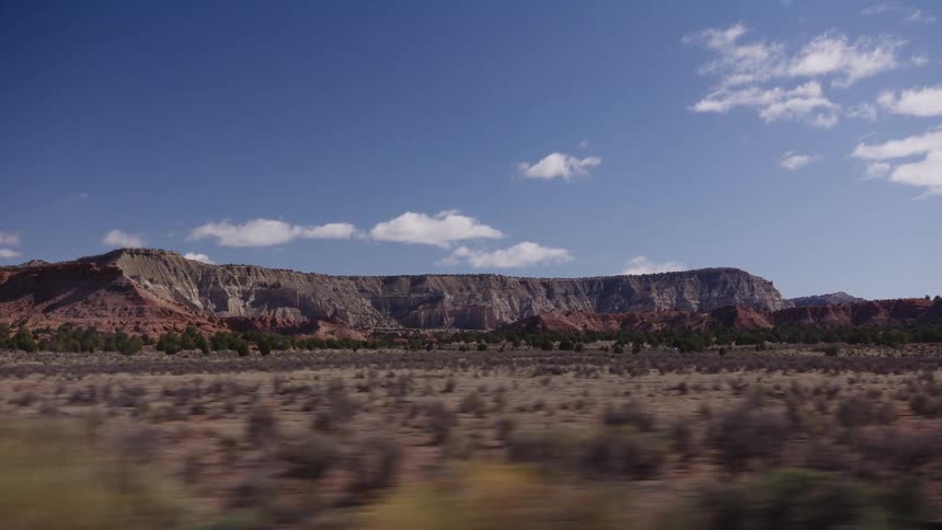 A scenic drive through a vast desert valley showcases majestic red and grey rock formations under a clear blue sky