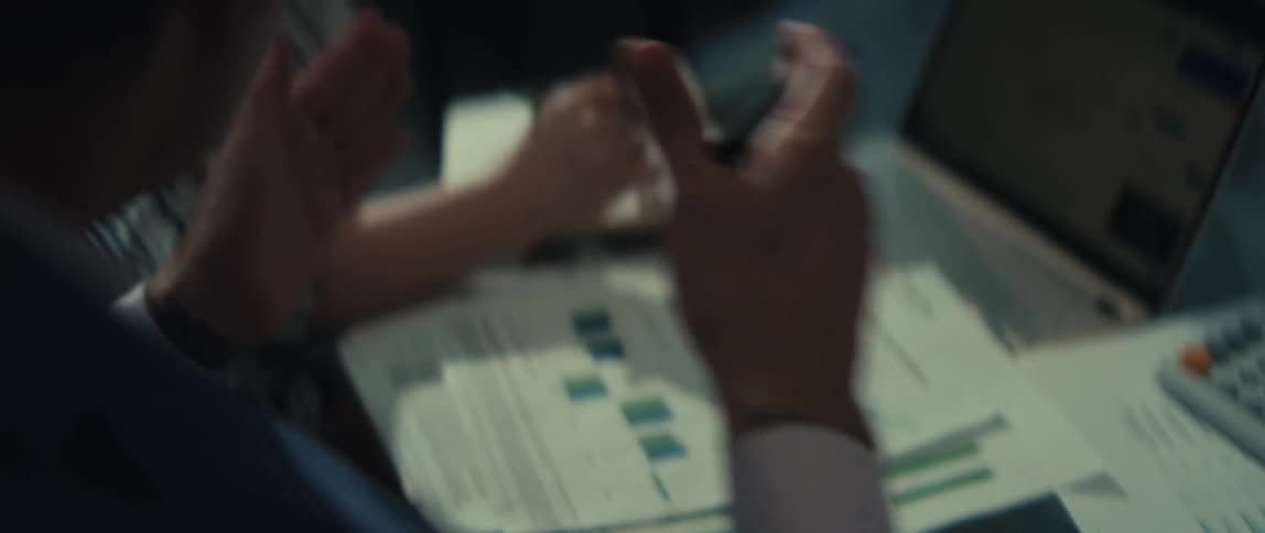Close-up of two colleagues analyzing financial charts on a laptop and printed reports while discussing strategy