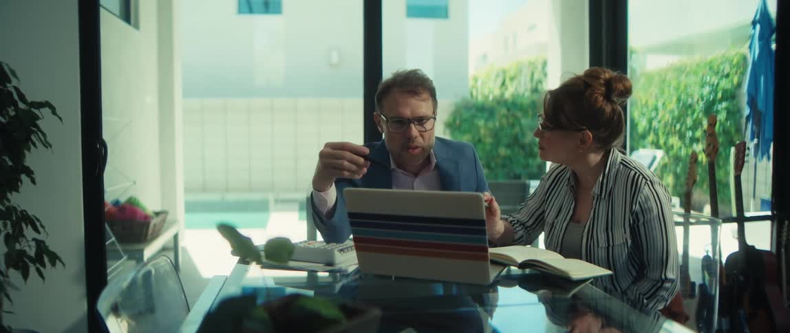 A man and woman collaborate on a project, looking at a laptop and taking notes in a modern, naturally lit room
